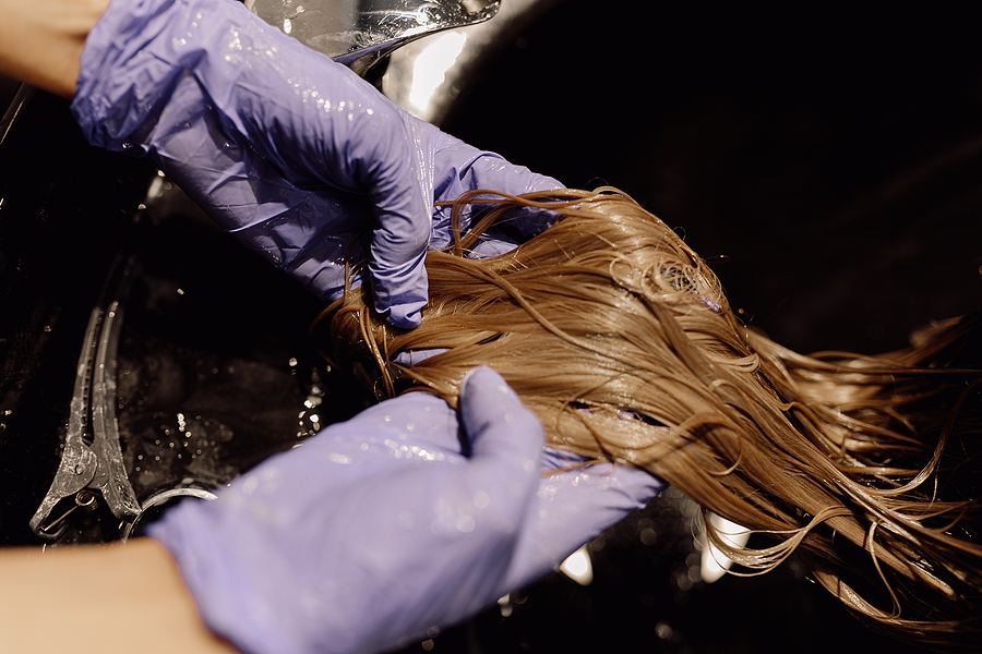 Caring for Synthetic Wigs in Humid Weather, Cropped photo of woman hairdresser hairstylist beautician wearing blue rubber gloves washing long dark hairpiece wig.